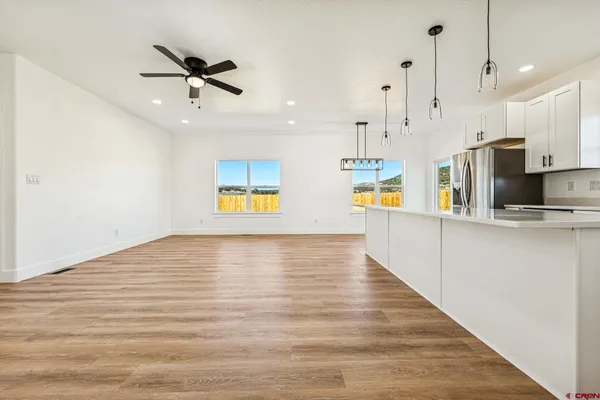a view of an empty room and kitchen with wooden floor