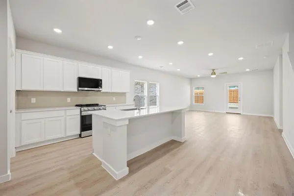 a large white kitchen with kitchen island a sink wooden floor and stainless steel appliances