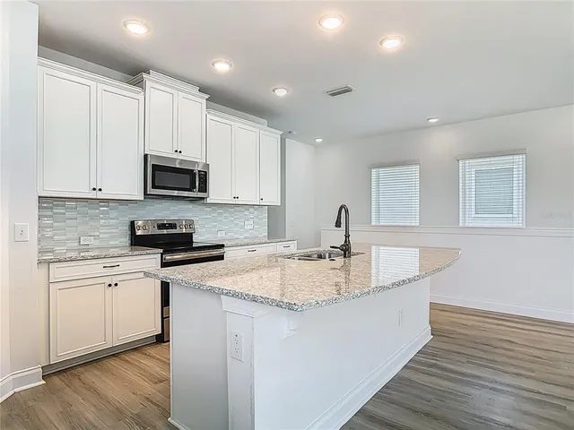 a large kitchen with stainless steel appliances granite countertop a sink a stove a microwave a center island and cabinets