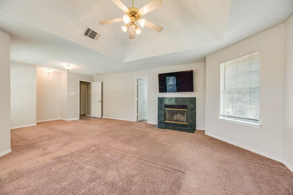 5610 Eagle Rock Road Arlington, TX 76017 - Photo 21 of 33 Spacious interior featuring a vaulted ceiling with a ceiling fan, a fireplace with a dark green surround, and light-colored carpeting