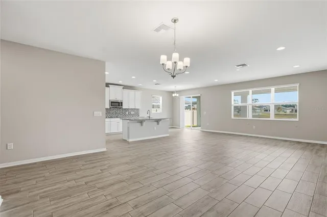 a view of an empty room with wooden floor and kitchen view