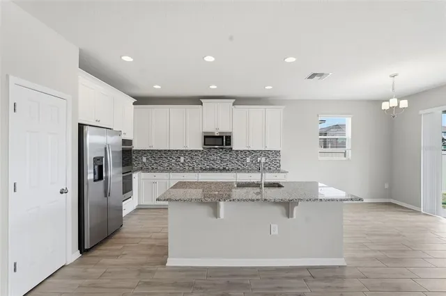 a large kitchen with stainless steel appliances granite countertop a stove a refrigerator a sink and white cabinets with wooden floor