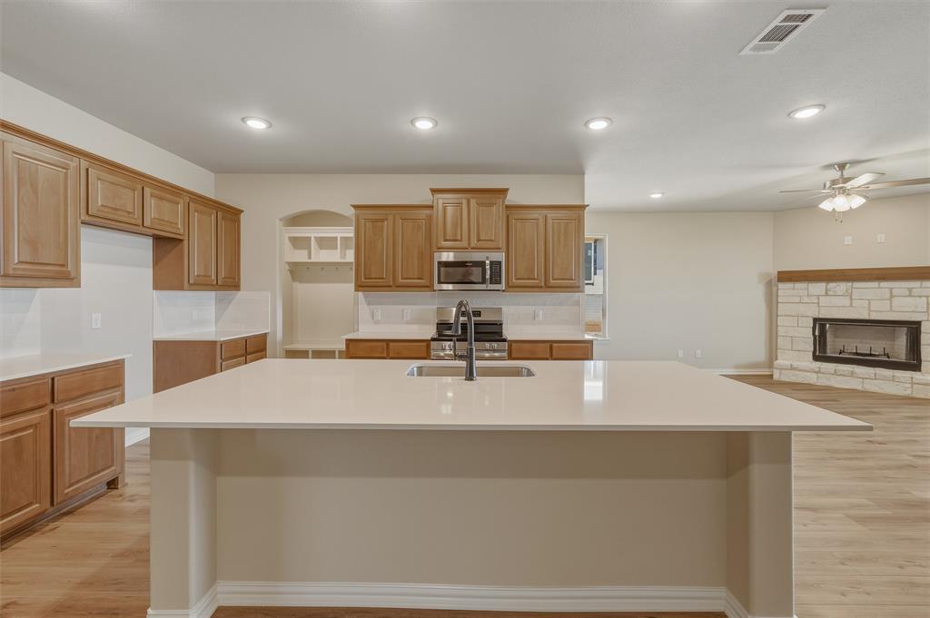 1209 Colca Drive Springtown, TX 76082 - Photo 8 of 24 Kitchen island with an undermount sink, quartz countertop, wood-finish cabinetry, stainless steel appliances, and wood-finish flooring