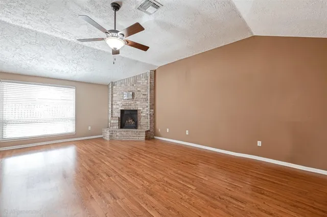 a view of an empty room with wooden floor fireplace and a window