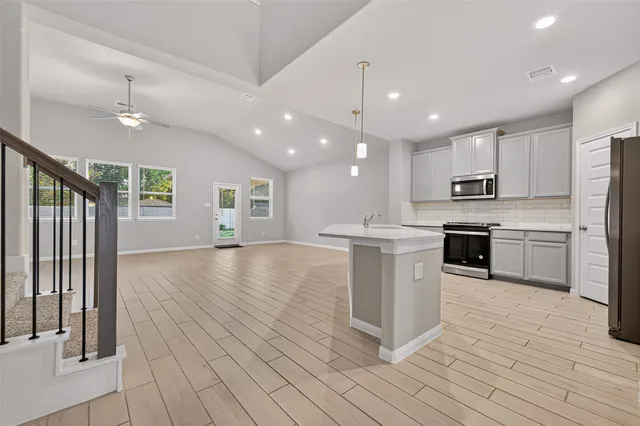 a large kitchen with a center island wooden floor stainless steel appliances and cabinets