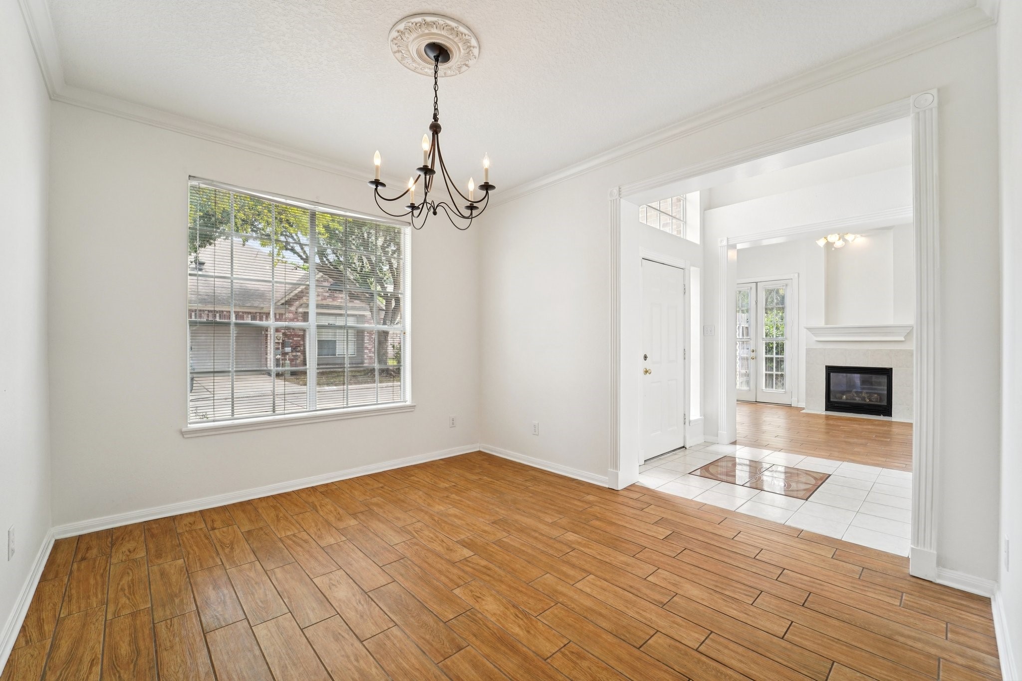 14420 Walters Road, Unit 55 Houston, TX 77014 - Photo 17 of 35 This photo showcases a bright, open living space with wood-like flooring and a large window providing natural light. It features a classic chandelier and leads into a room with a fireplace and French doors, creating a warm and inviting atmosphere.