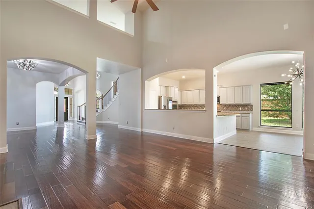 a view of an empty room with wooden floor and a kitchen view