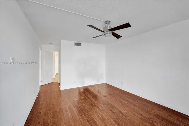 an empty room with wooden floor and a ceiling fan