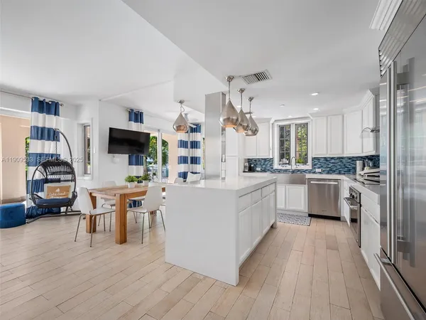a large white kitchen with cabinets a sink a counter space stainless steel appliances and windows
