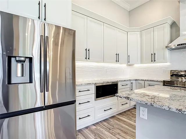 a kitchen with granite countertop a refrigerator a stove and white cabinets with wooden floor