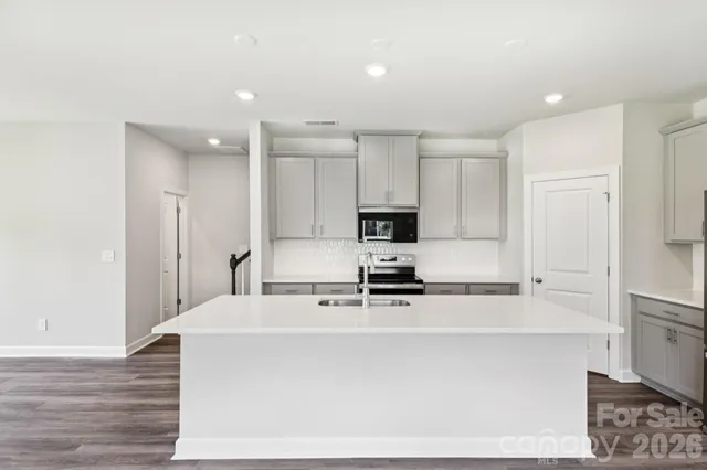 a kitchen with stainless steel appliances a stove top oven a sink a refrigerator white cabinets and wooden floor