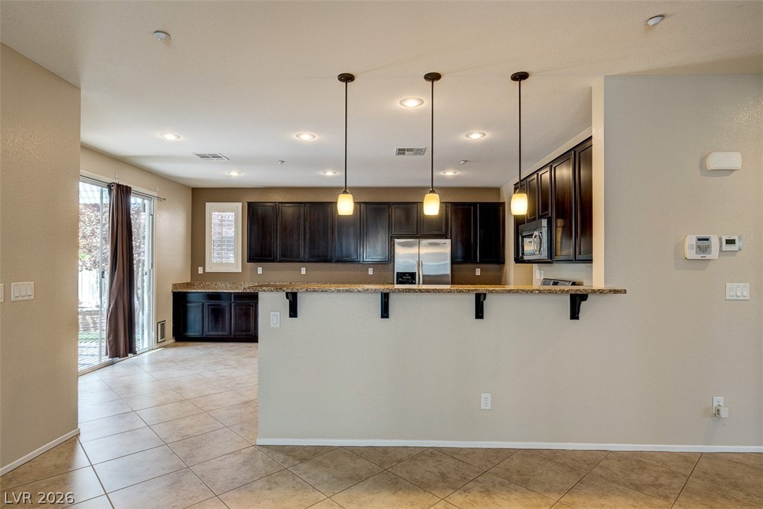 3199 Subtle Color Avenue Henderson, NV 89044 - Photo 12 of 46 Kitchen featuring a peninsula, a kitchen bar, stainless steel appliances, and dark wood finish cabinets