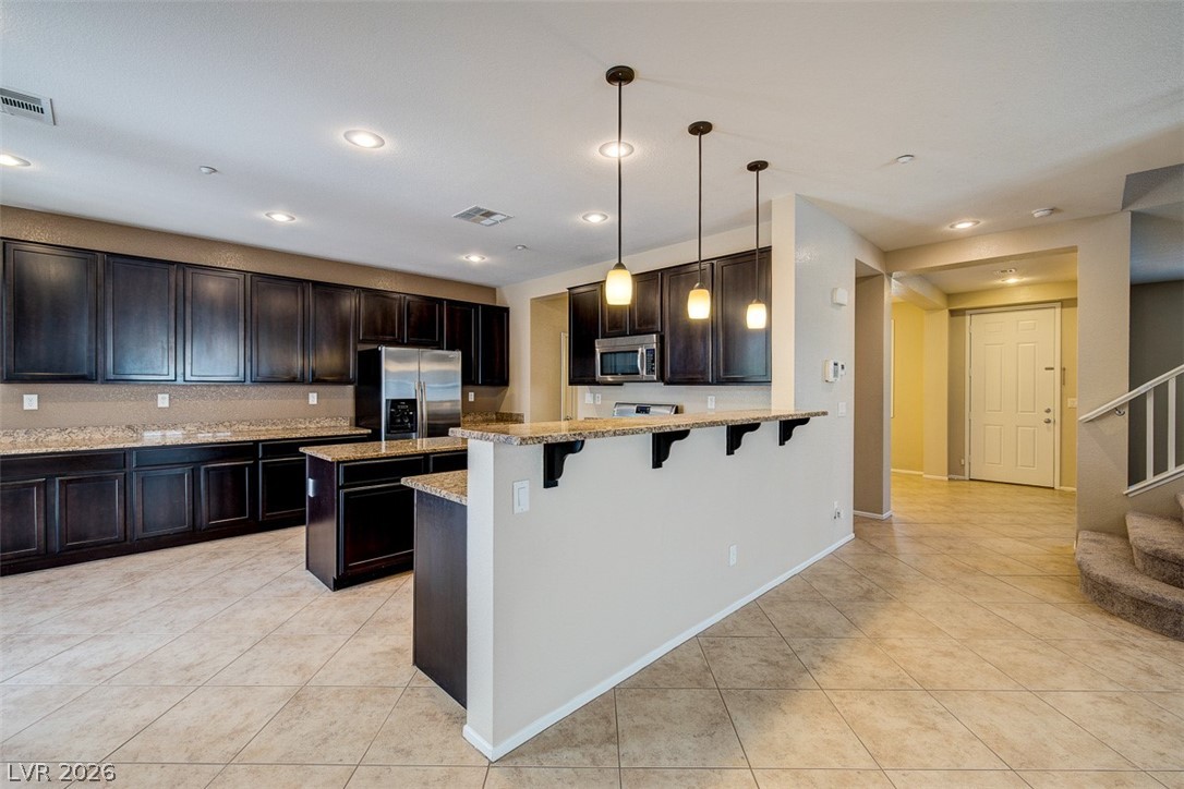 3199 Subtle Color Avenue Henderson, NV 89044 - Photo 13 of 46 Kitchen with a breakfast bar, hanging light fixtures, a peninsula, light tile patterned floors, and stainless steel appliances