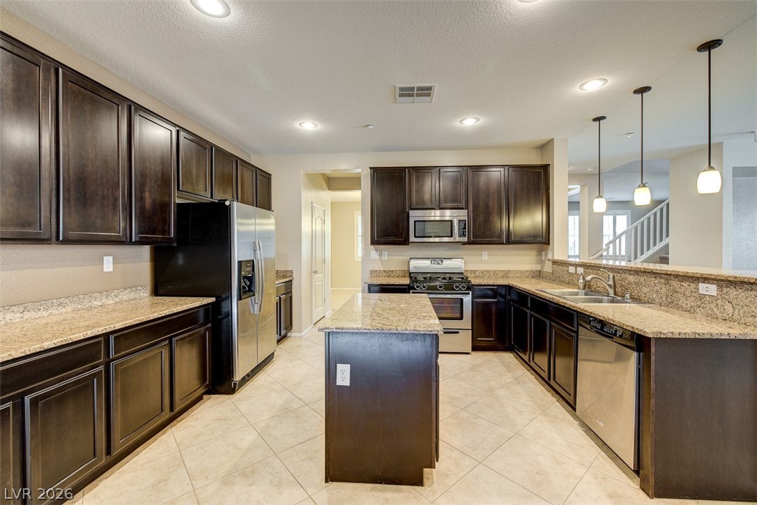 3199 Subtle Color Avenue Henderson, NV 89044 - Photo 14 of 46 Kitchen with dark wood finish cabinets, stainless steel appliances, a kitchen island, light stone countertops, and a peninsula