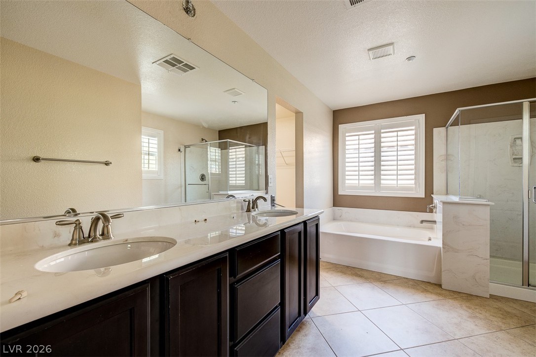 3199 Subtle Color Avenue Henderson, NV 89044 - Photo 25 of 46 Full bath featuring a garden tub, double vanity, a shower stall, light tile patterned flooring, and a textured ceiling