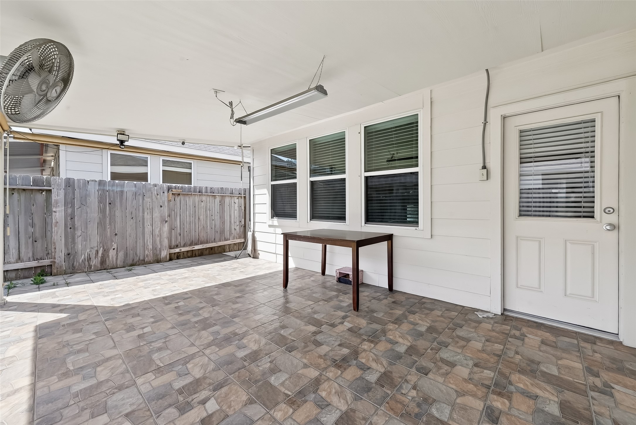 7631 Granite Terrace Lane Houston, TX 77083 - Photo 40 of 46 This photo shows a spacious, tiled covered patio with a ceiling fan, ample natural light, and a wooden fence for privacy. Ideal for outdoor relaxation or entertaining.