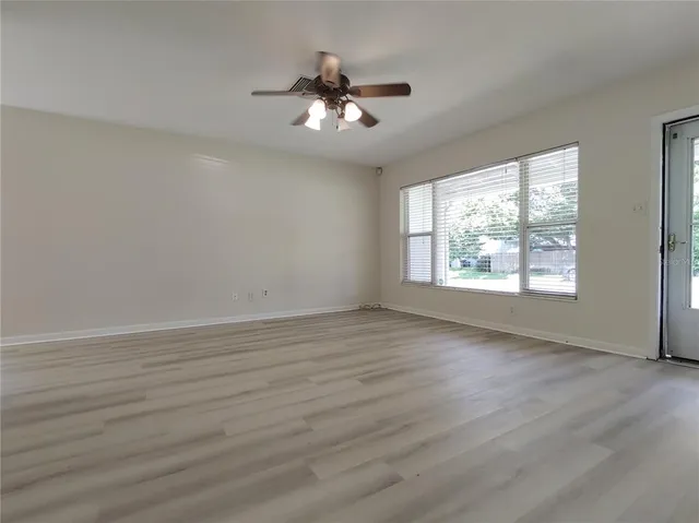 an empty room with wooden floor chandelier fan and windows