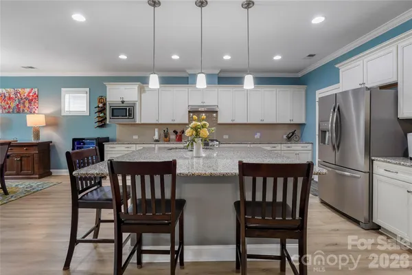 a kitchen with stainless steel appliances granite countertop a dining table chairs refrigerator and microwave