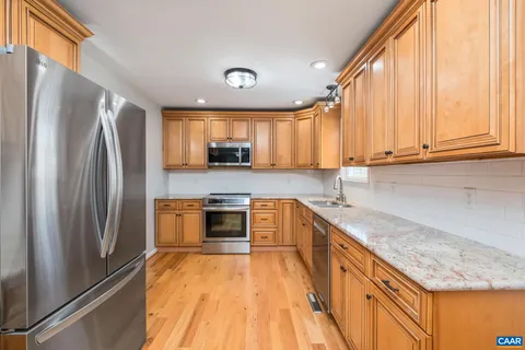 a kitchen with stainless steel appliances granite countertop a refrigerator a sink dishwasher a stove and white countertops with wooden floor