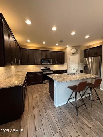 a kitchen with stainless steel appliances kitchen island granite countertop a table chairs stove and refrigerator