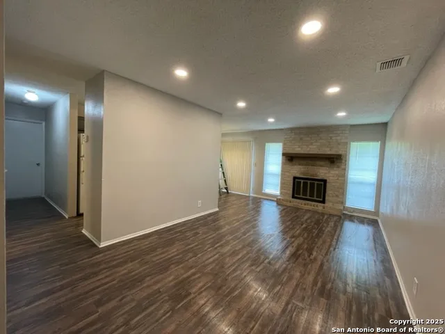 an empty room with wooden floor fireplace and windows