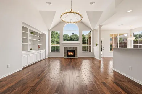 an empty room with wooden floor fireplace and windows