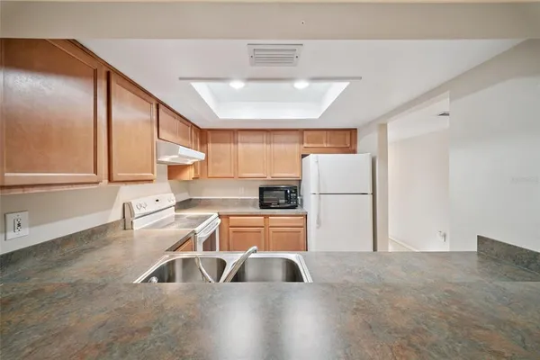 a kitchen with granite countertop a refrigerator a sink and white cabinets