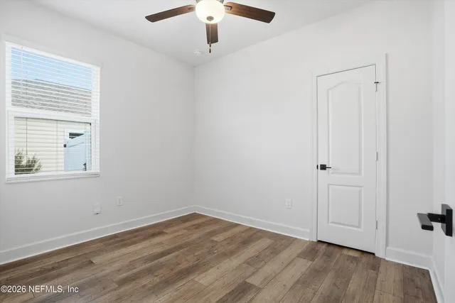 an empty room with wooden floor chandelier fan and windows