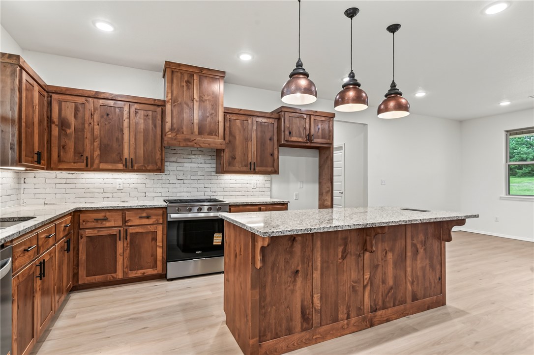 6138 New Hope Road Hackett, AR 72937 - Photo 50 of 56 Kitchen featuring wood cabinetry, a center island with pendant lighting, a stainless steel range, and a white brick-finish backsplash