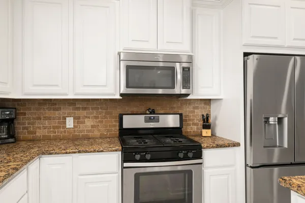 a kitchen with stainless steel appliances granite countertop white cabinets a refrigerator a stove a microwave and a sink