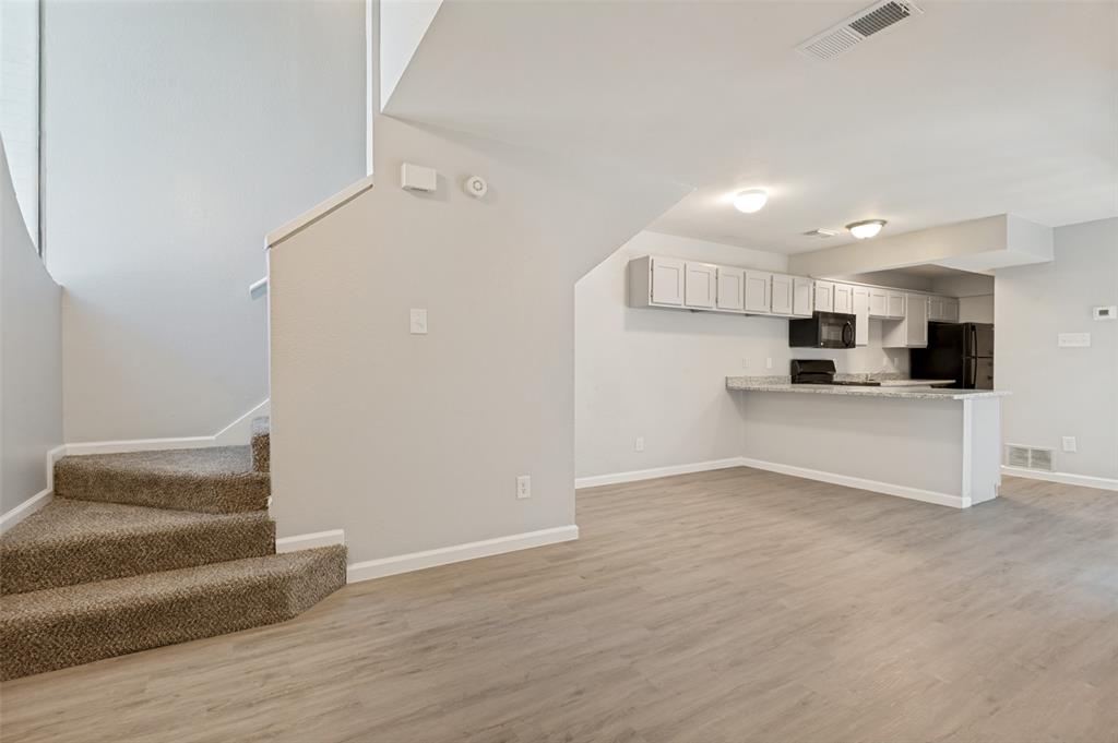 622 West Union Bower Road Irving, TX 75061 - Photo 7 of 13 Open-concept living area featuring wood-finish flooring, a breakfast bar with stone-finish countertop, white cabinetry, and black appliances