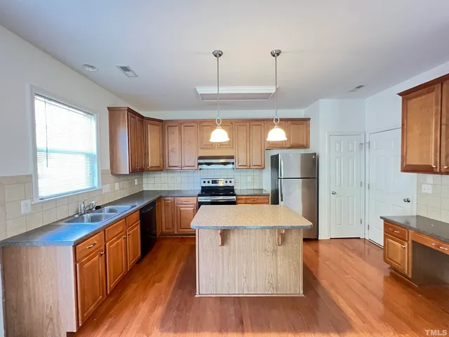 a large kitchen with stainless steel appliances kitchen island granite countertop a stove a refrigerator a sink dishwasher a dining table and chairs with wooden floor