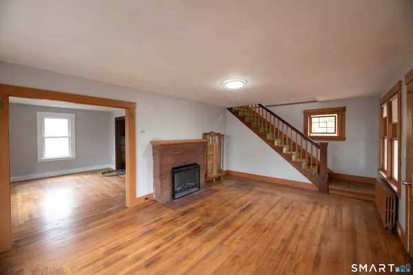 a view of an empty room with wooden floor fireplace and a window