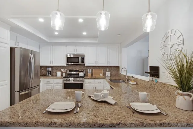 a kitchen with stainless steel appliances granite countertop a stove a refrigerator a couch a dining table and chairs with wooden floor