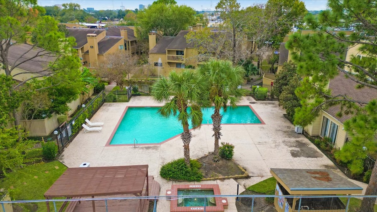 3502 Ocee Street, Unit 3502 Houston, TX 77063 - Photo 25 of 28 This photo shows a community pool area surrounded by residential buildings. The pool is large, with a spacious deck featuring lounge chairs and a few palm trees nearby. The area is fenced and well-maintained, offering a relaxing outdoor space for residents.