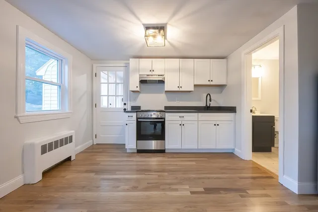 a kitchen with stainless steel appliances granite countertop a stove a sink dishwasher a refrigerator and white cabinets with wooden floor