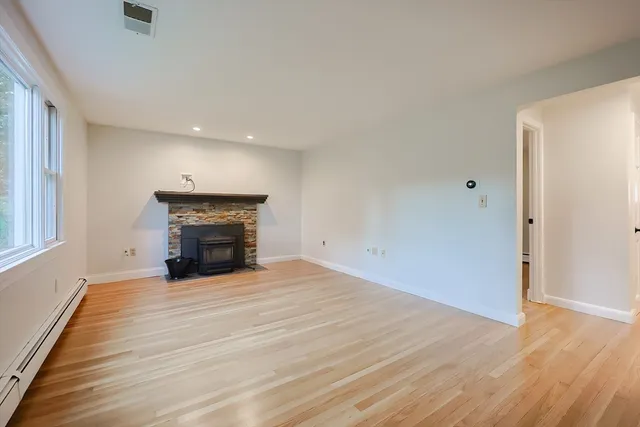 an empty room with wooden floor fireplace and windows