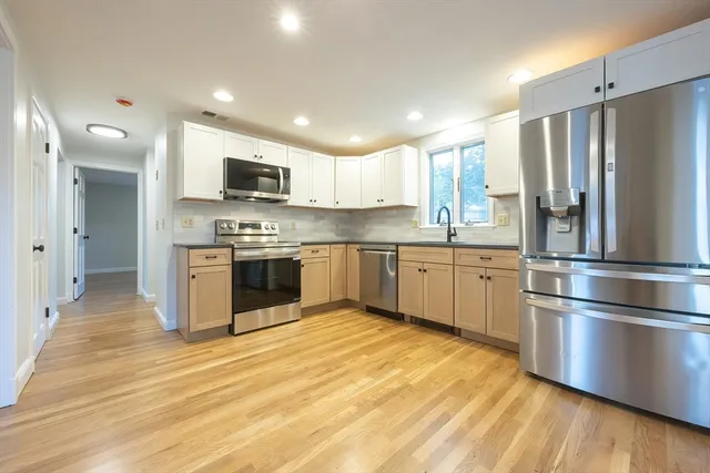 a kitchen with stainless steel appliances granite countertop a stove top oven a refrigerator and a sink with wooden floor