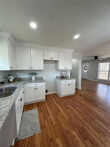 a kitchen with stainless steel appliances granite countertop a sink dishwasher a refrigerator and white cabinets with wooden floor