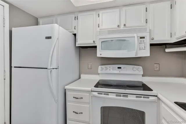 a white refrigerator freezer and a stove sitting inside of a kitchen with granite countertop white cabinets