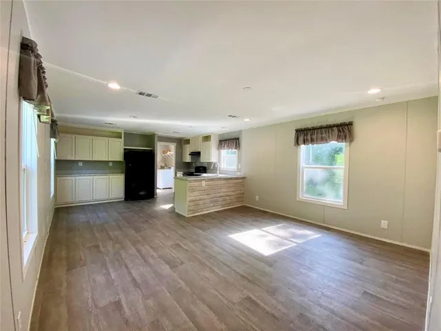 a view of empty room with wooden floor and kitchen