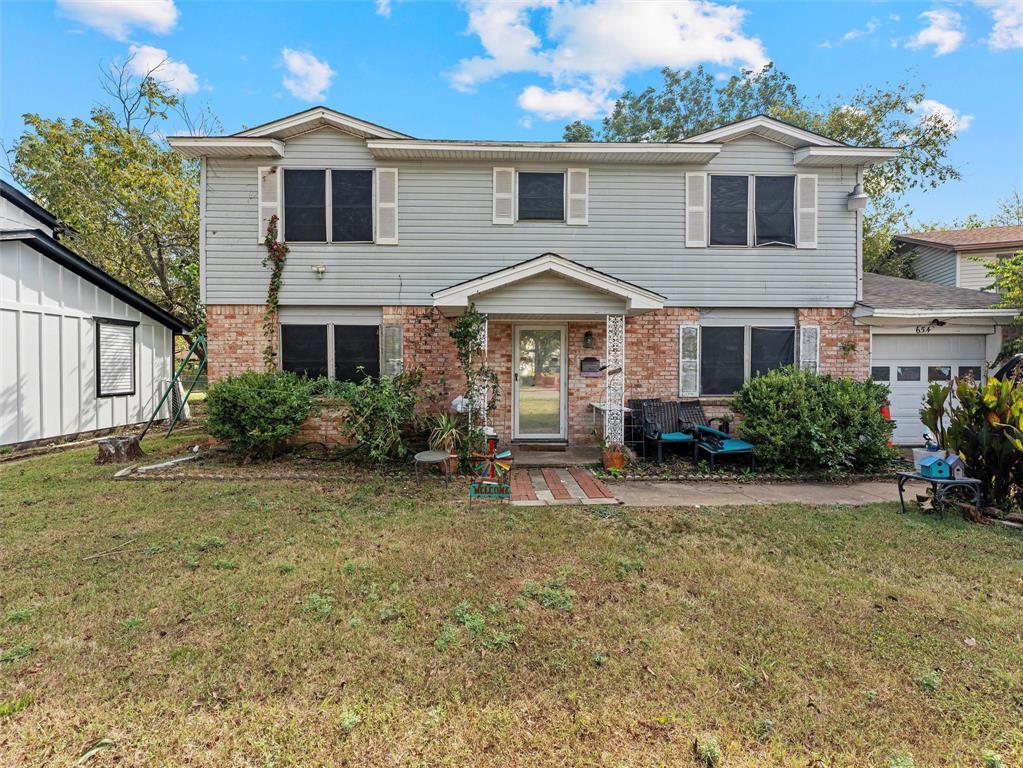 a white house that has a small yard and large trees with wooden fence