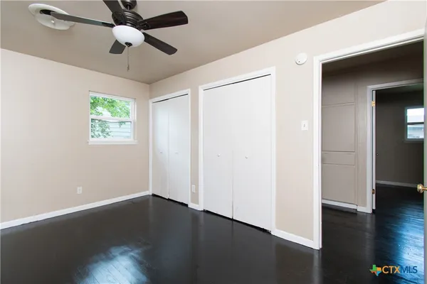 an empty room with wooden floor chandelier fan and windows