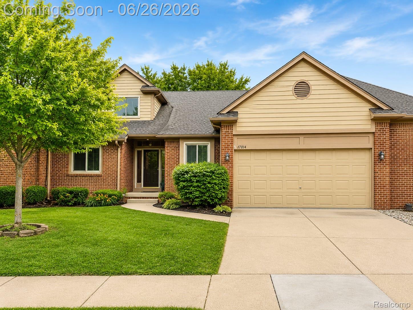 Brick and siding exterior featuring a two-car garage, mature landscaping, a paved driveway, and a concrete walkway