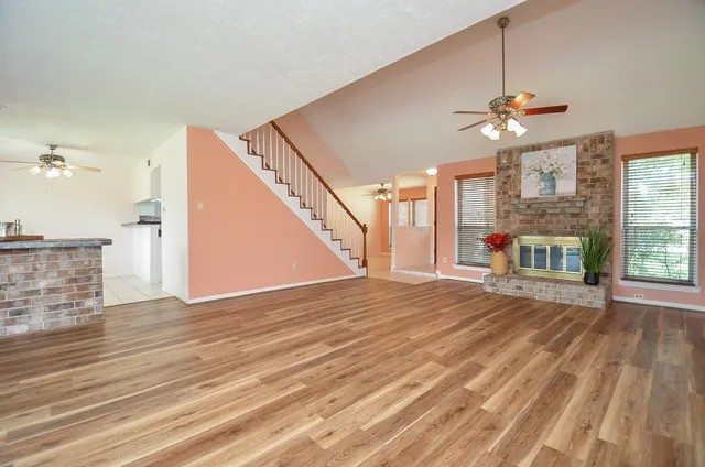 a view of an empty room with wooden floor and a ceiling fan