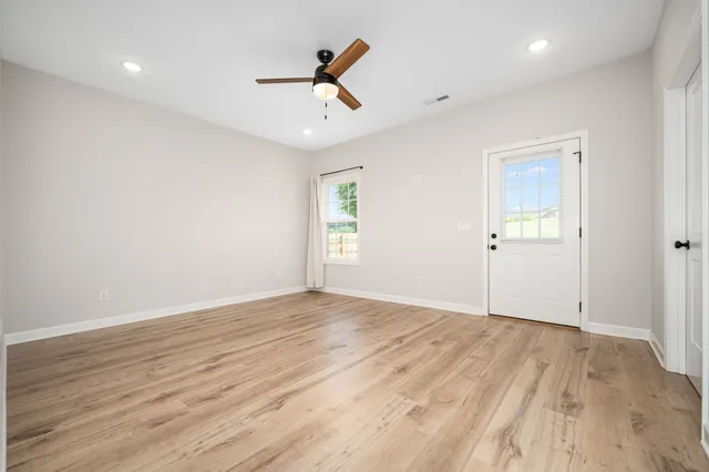 an empty room with wooden floor ceiling fan and windows