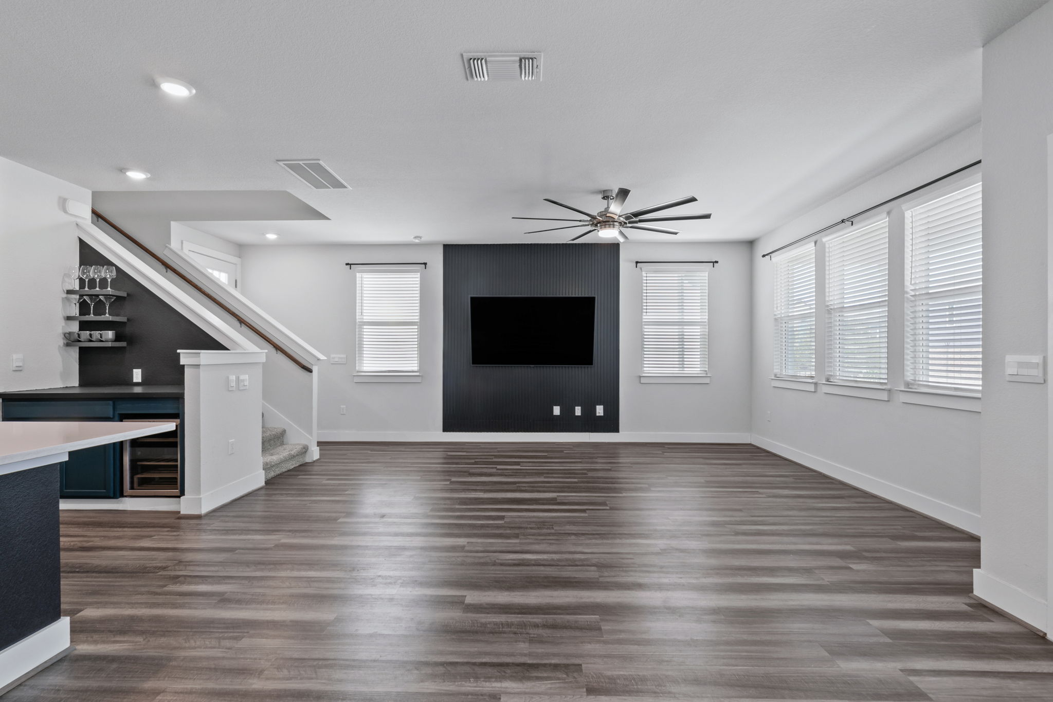 7312 Travertine Spring Drive Austin, TX 78744 - Photo 14 of 32 A contemporary great room featuring wide plank flooring and a sleek beverage bar under the stairs.