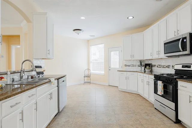 a large white kitchen with stainless steel appliances granite countertop a stove a sink a refrigerator and white cabinets