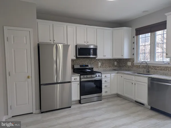 a kitchen with stainless steel appliances granite countertop a refrigerator stove a sink and white cabinets