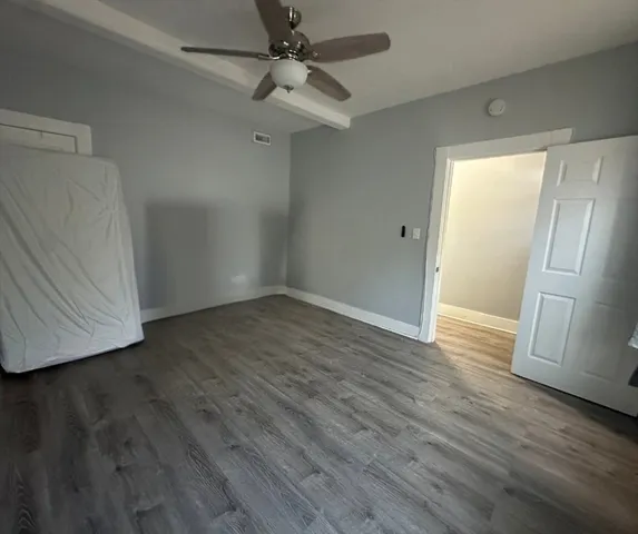 a view of an empty room with wooden floor and a ceiling fan